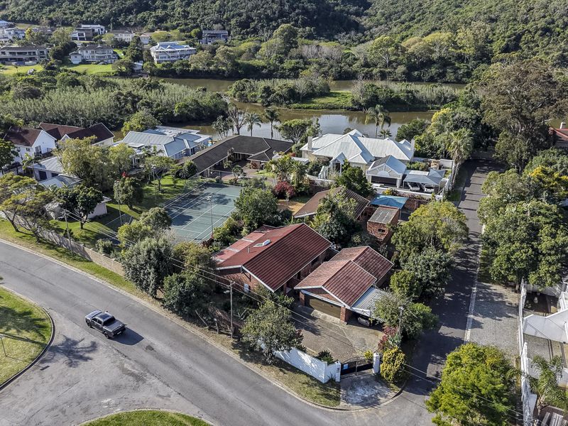 Aerial view of a residential property featuring a tennis court, swimming pool, and tiled roof structures situated in a landscaped estate setting.