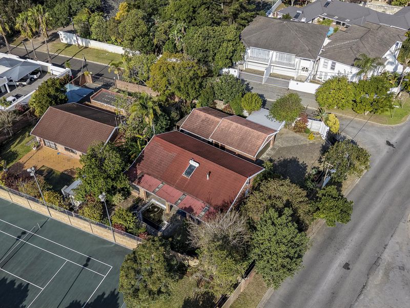 Aerial view of a residential property featuring a tiled roof with solar heating, a private tennis court, and a paved driveway.