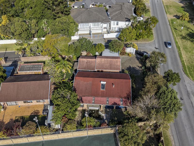 Aerial view of the property showing the main dwelling, tiled roof with solar heating, paved driveway, and a private tennis court.