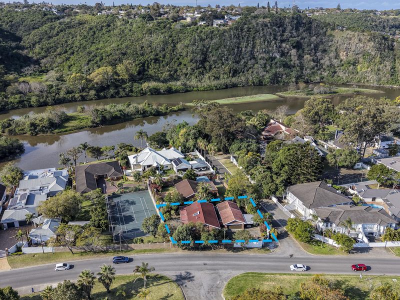 Aerial view of a residential property featuring a tennis court, river frontage, and established garden surroundings in a scenic neighborhood.