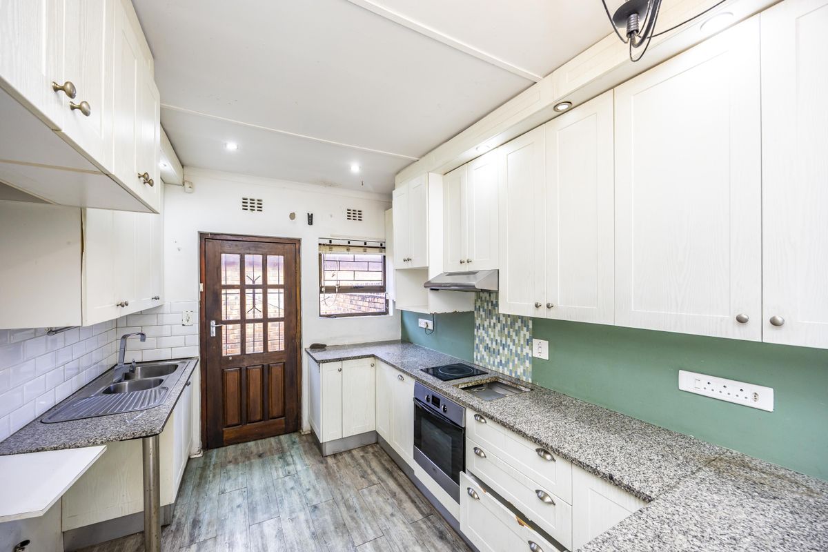 A functional kitchen featuring white cabinetry, granite countertops, built-in oven and hob, and a tiled backsplash with direct access to the exterior.