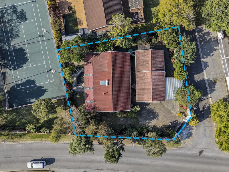 Aerial view of the property showing the main dwelling, tiled roof with solar heater, paved driveway, and surrounding garden area.