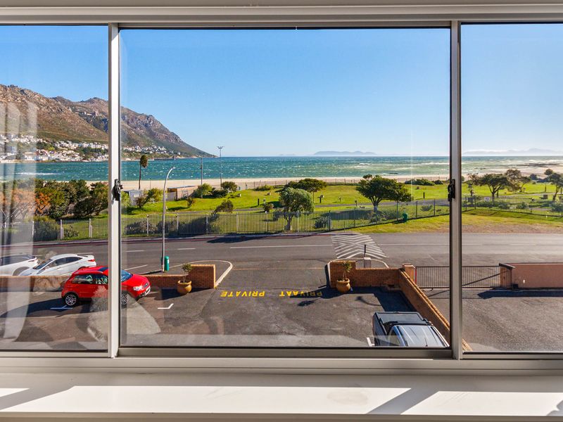A clear view of the beach, ocean, and mountains framed through a large sliding window.