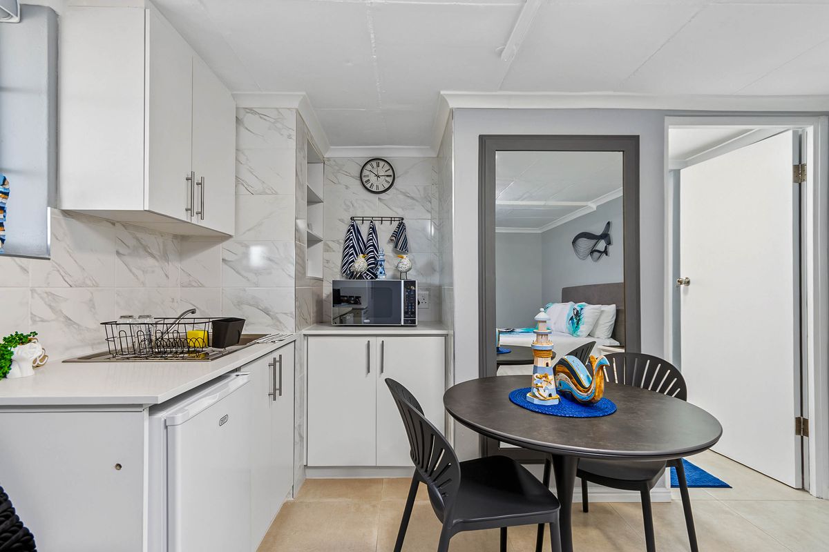 Compact kitchen featuring white cabinetry, marble-look tile backsplash, and tiled flooring, seamlessly integrated into the living space.