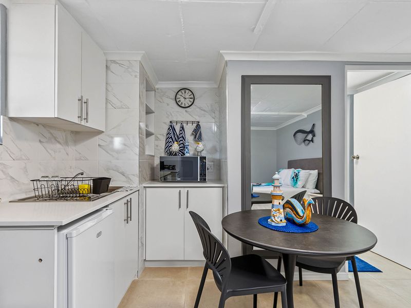 Compact kitchen featuring white cabinetry, marble-look tile backsplash, and tiled flooring, seamlessly integrated into the living space.