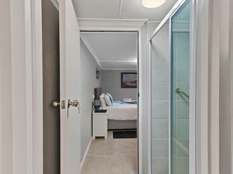 A view from a bathroom looking into an adjacent bedroom, featuring a glass shower enclosure and neutral tiled flooring.