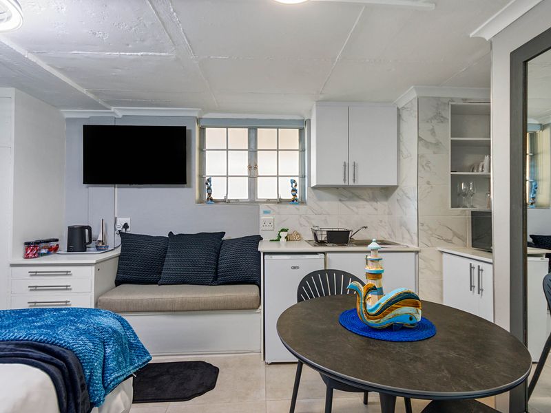 Compact open-plan living area featuring a kitchenette with marble-look backsplash, built-in cabinetry, and integrated bench seating.
