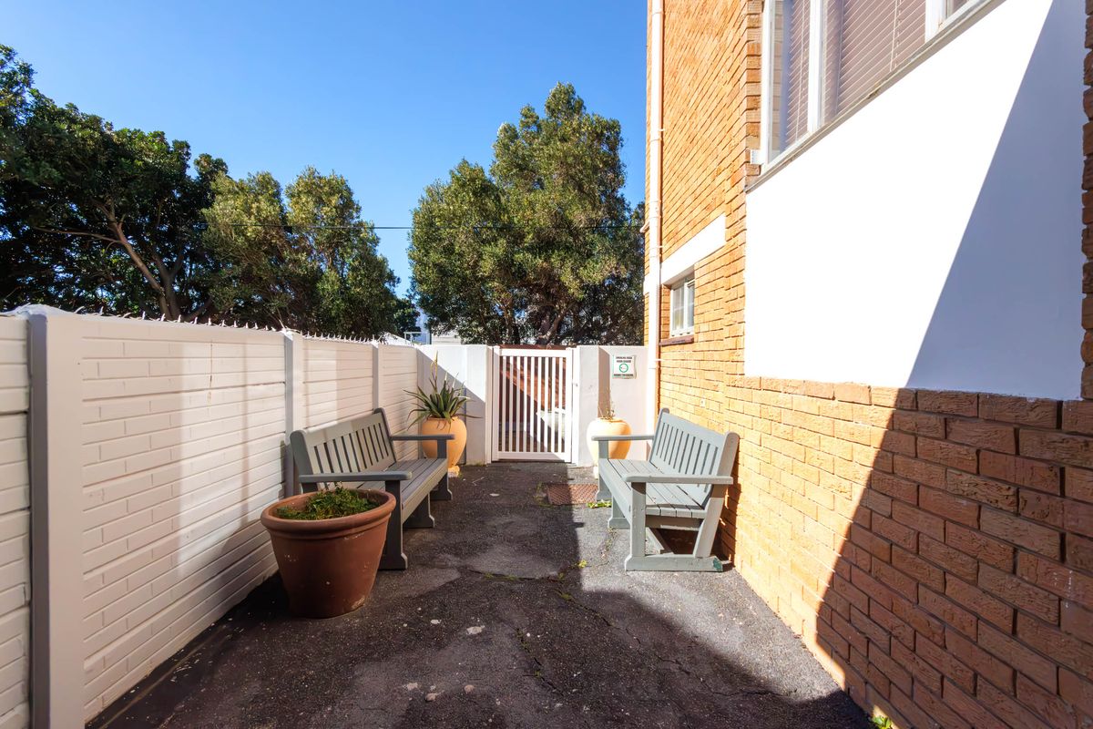 A private rear courtyard featuring a paved surface, brick boundary walls with security spikes, and a pedestrian access gate.