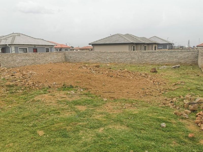 A vacant residential plot featuring a perimeter brick wall and partially cleared ground, ready for development.