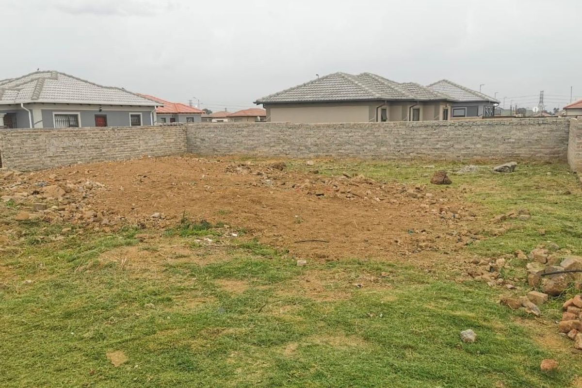 A vacant residential plot featuring a perimeter brick wall and partially cleared ground, ready for development.