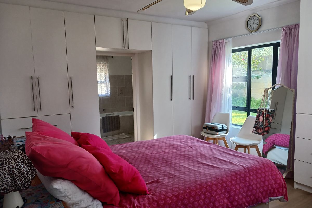 A well-lit bedroom featuring extensive built-in cabinetry, a ceiling fan, and an en-suite bathroom access, with large windows providing natural light.