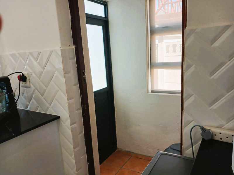 A functional scullery or utility area featuring a modern herringbone tile backsplash, black granite countertops, and direct access to the exterior.