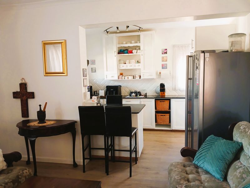 Open plan kitchen area featuring white cabinetry, a breakfast bar, subway tile backsplash, and laminate flooring, seamlessly connected to the living space.