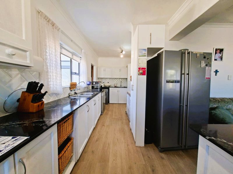 A functional kitchen featuring white cabinetry, dark laminate countertops, a herringbone tile backsplash, and light wood-look laminate flooring.