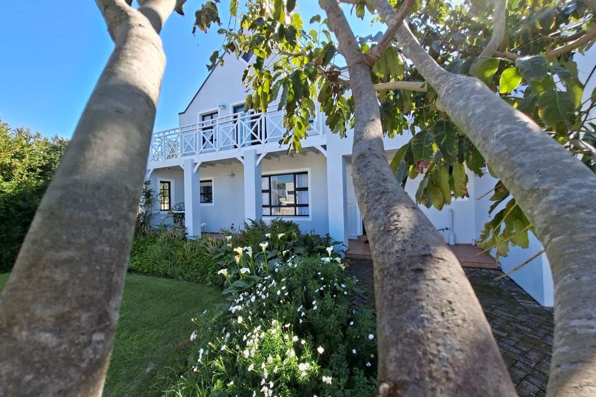 A view of the rear elevation featuring a white gabled facade, a first-floor balcony with timber railings, and a well-maintained garden.
