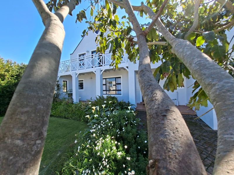 A view of the rear elevation featuring a white gabled facade, a first-floor balcony with timber railings, and a well-maintained garden.