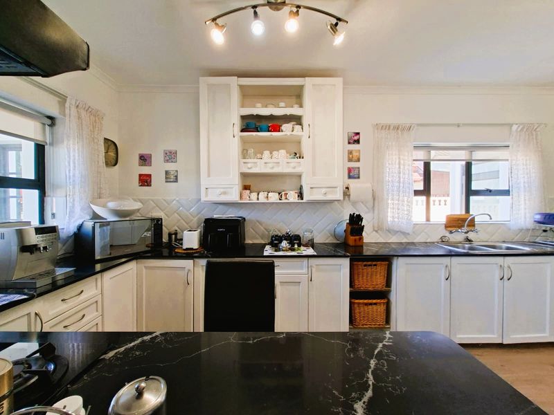 A well-maintained kitchen featuring white cabinetry, contrasting black marble-effect countertops, subway tile backsplash, and functional stainless steel sink and tap fixtures.