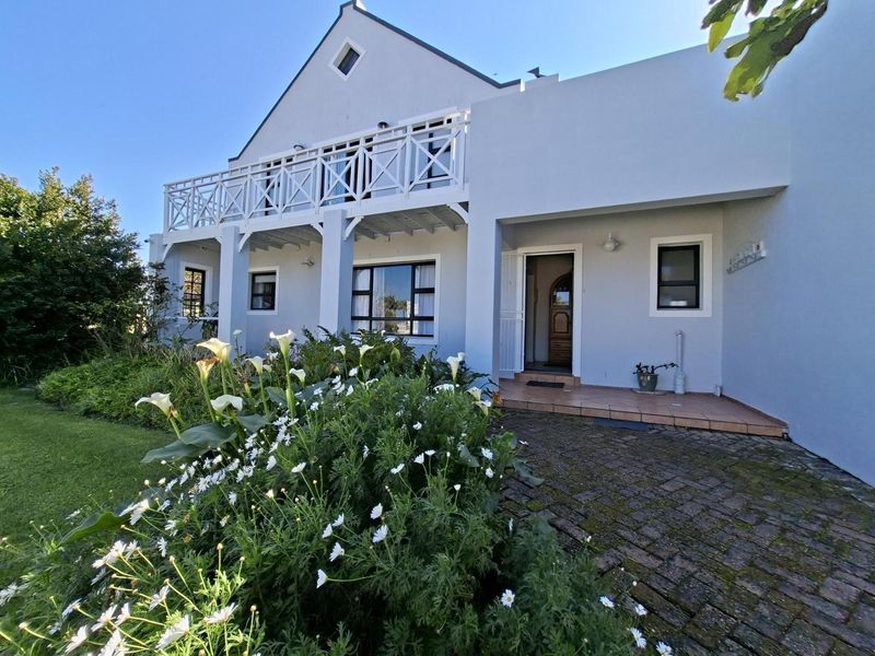 Front elevation of a Cape Dutch style house featuring a balcony, paved entrance area, and established garden.