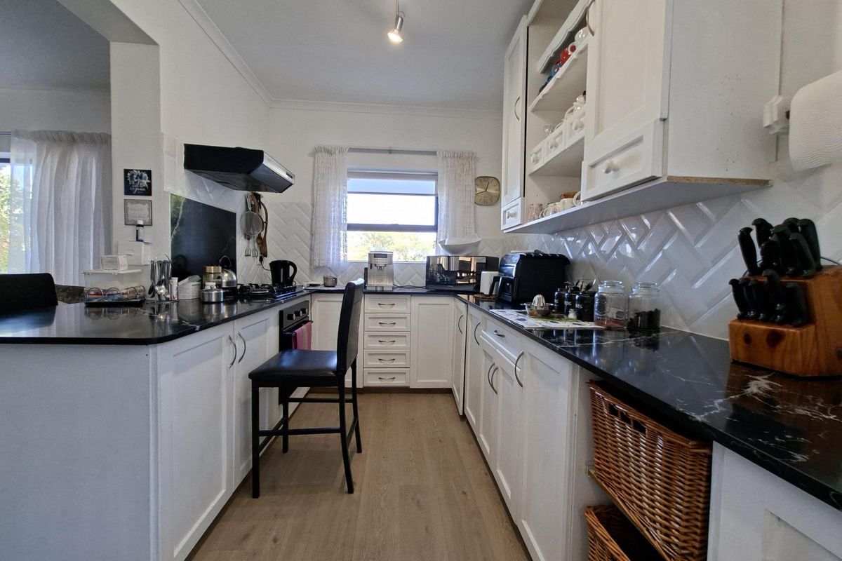 A well-maintained kitchen featuring white cabinetry, contrasting black stone countertops, a stylish herringbone tile backsplash, and modern laminate flooring.