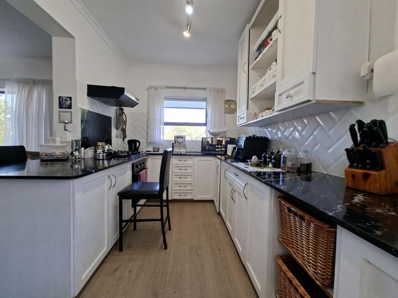 A well-maintained kitchen featuring white cabinetry, contrasting black stone countertops, a stylish herringbone tile backsplash, and modern laminate flooring.