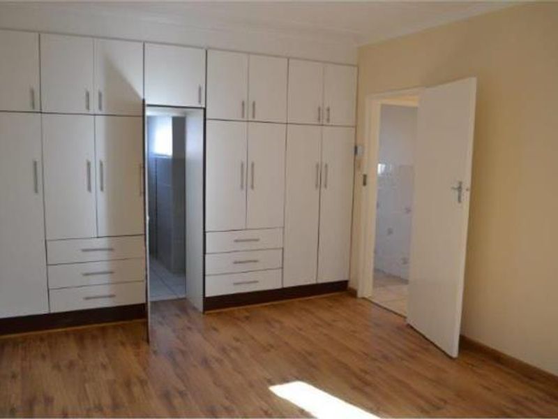 A clean, empty bedroom featuring extensive white built-in cupboards, laminate flooring, and direct access to an adjoining room.