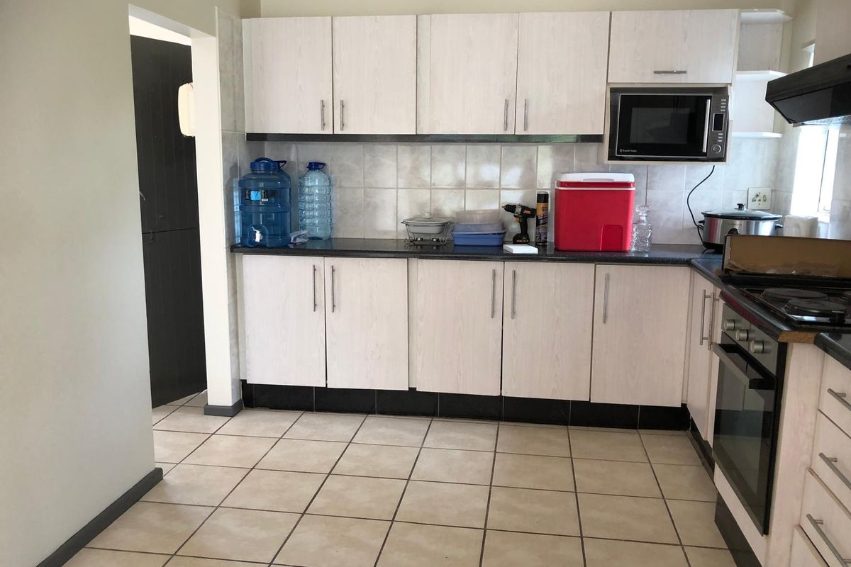 A functional kitchen featuring light-toned cabinetry, dark countertops, tiled backsplash, and integrated appliances including an oven and extractor fan.