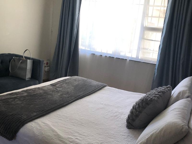 A standard bedroom featuring a window with security bars and fitted curtain rods.