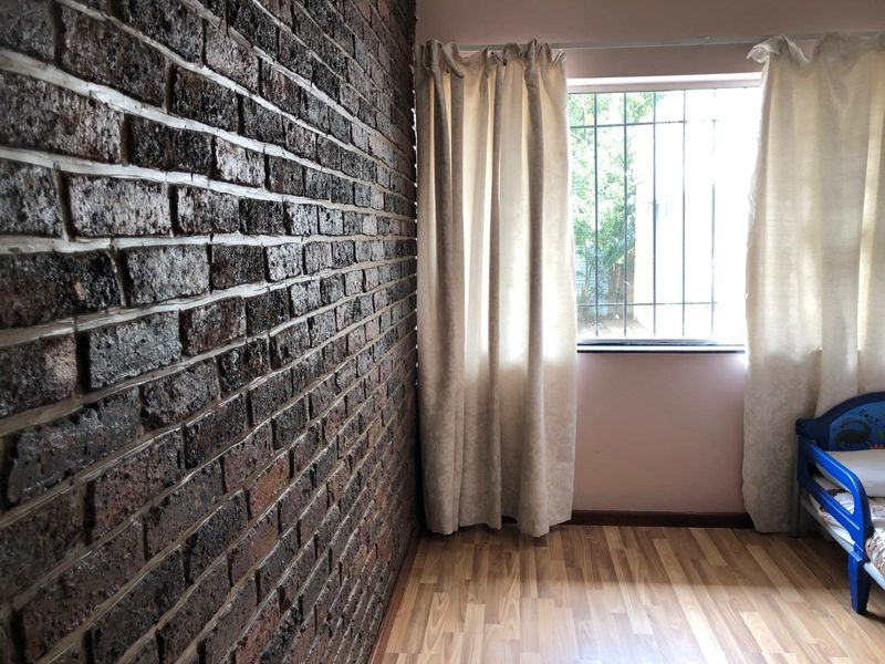 Bedroom featuring a prominent exposed brick feature wall, laminate flooring, and a window fitted with security bars.