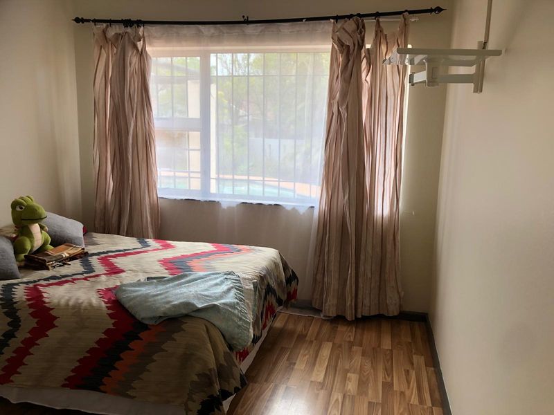 A functional bedroom featuring laminate flooring, a window with security bars, and a wall-mounted TV bracket.
