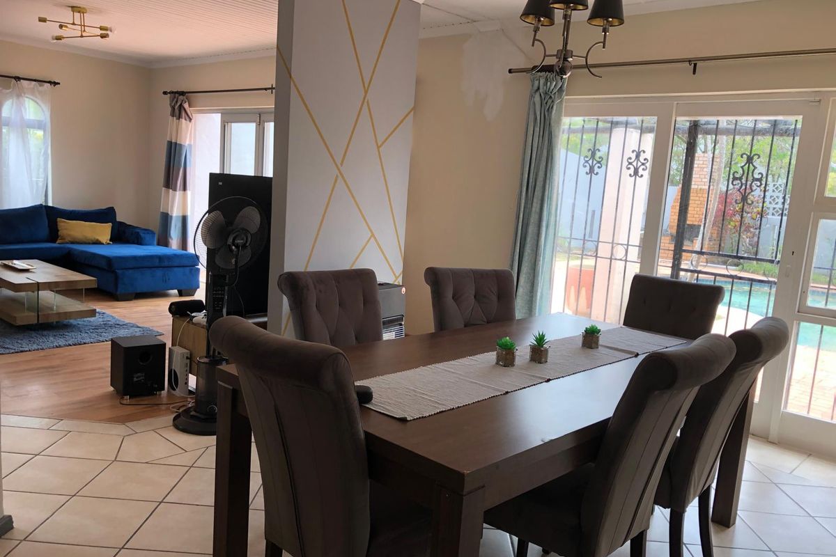 Open-plan living and dining area featuring tiled floors, a decorative feature wall, and sliding glass doors leading to the outdoor pool area.