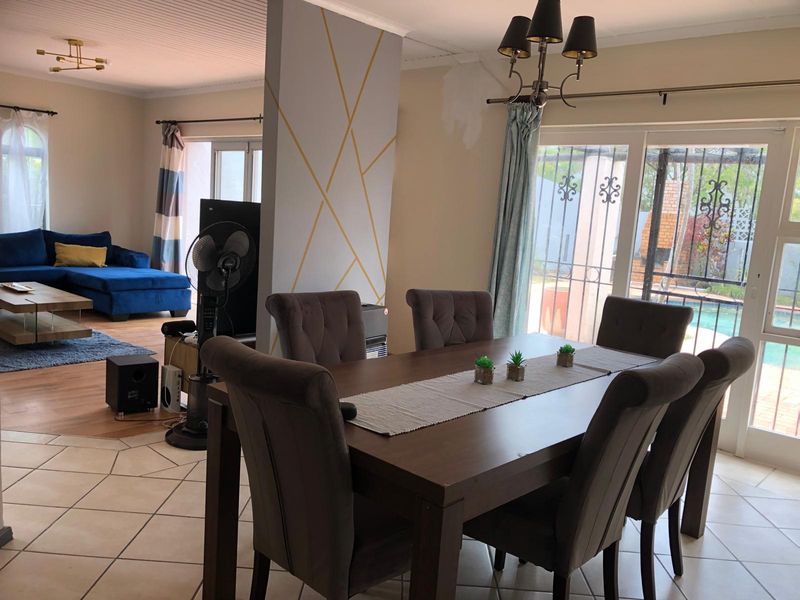 Open-plan living and dining area featuring tiled floors, a decorative feature wall, and sliding glass doors leading to the outdoor pool area.
