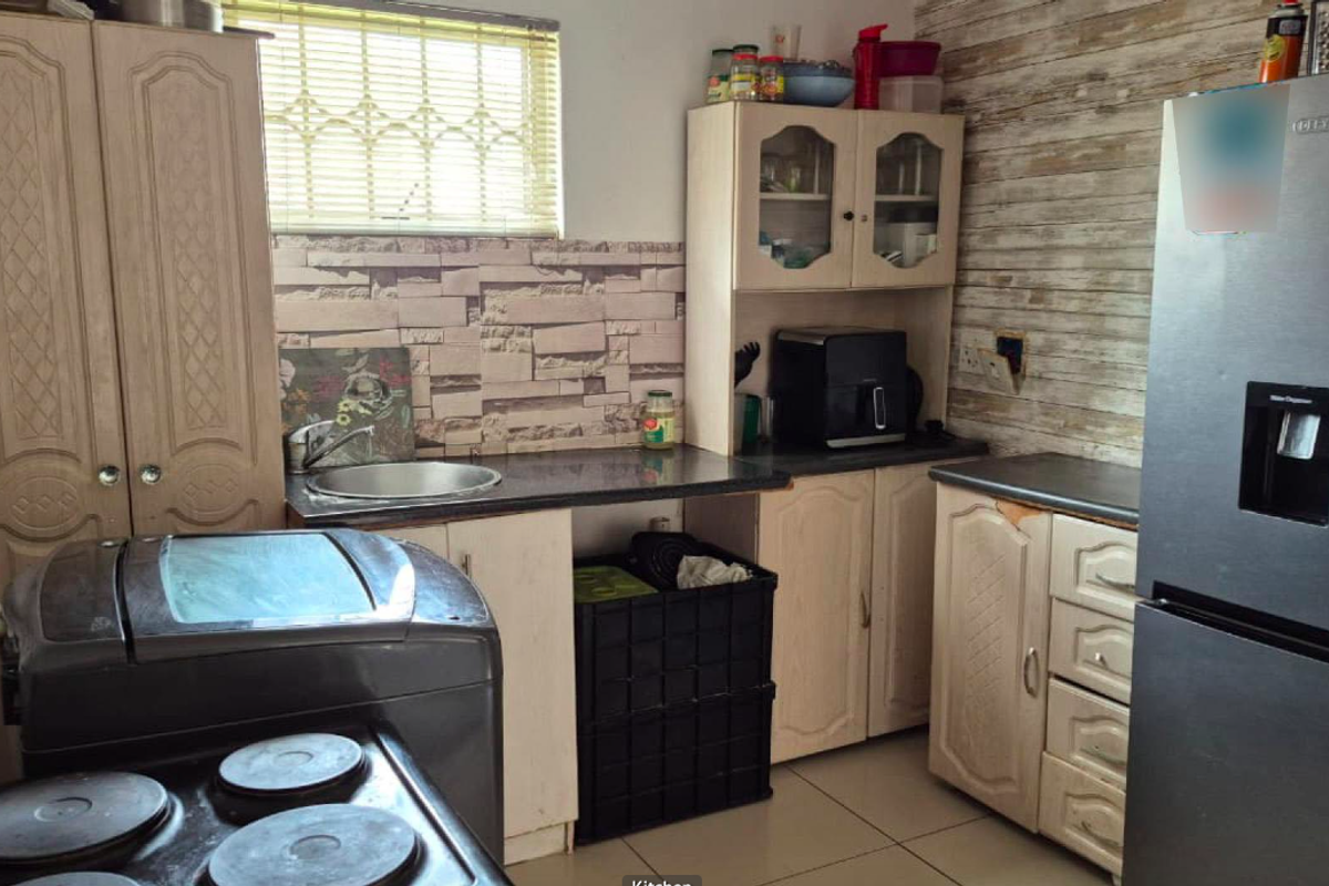 A functional kitchen featuring built-in cabinetry, laminate countertops, and a stainless steel sink, with a tiled backsplash and window blinds.
