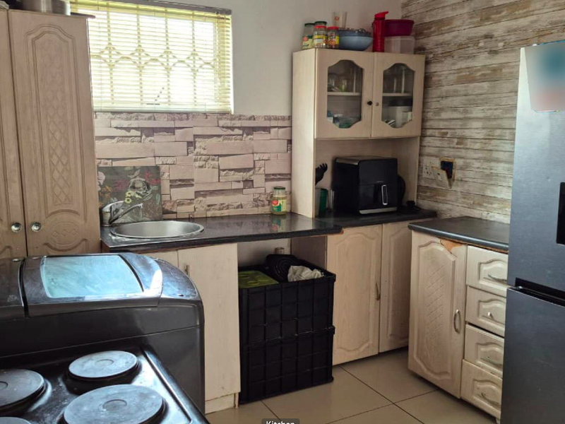 A functional kitchen featuring built-in cabinetry, laminate countertops, and a stainless steel sink, with a tiled backsplash and window blinds.