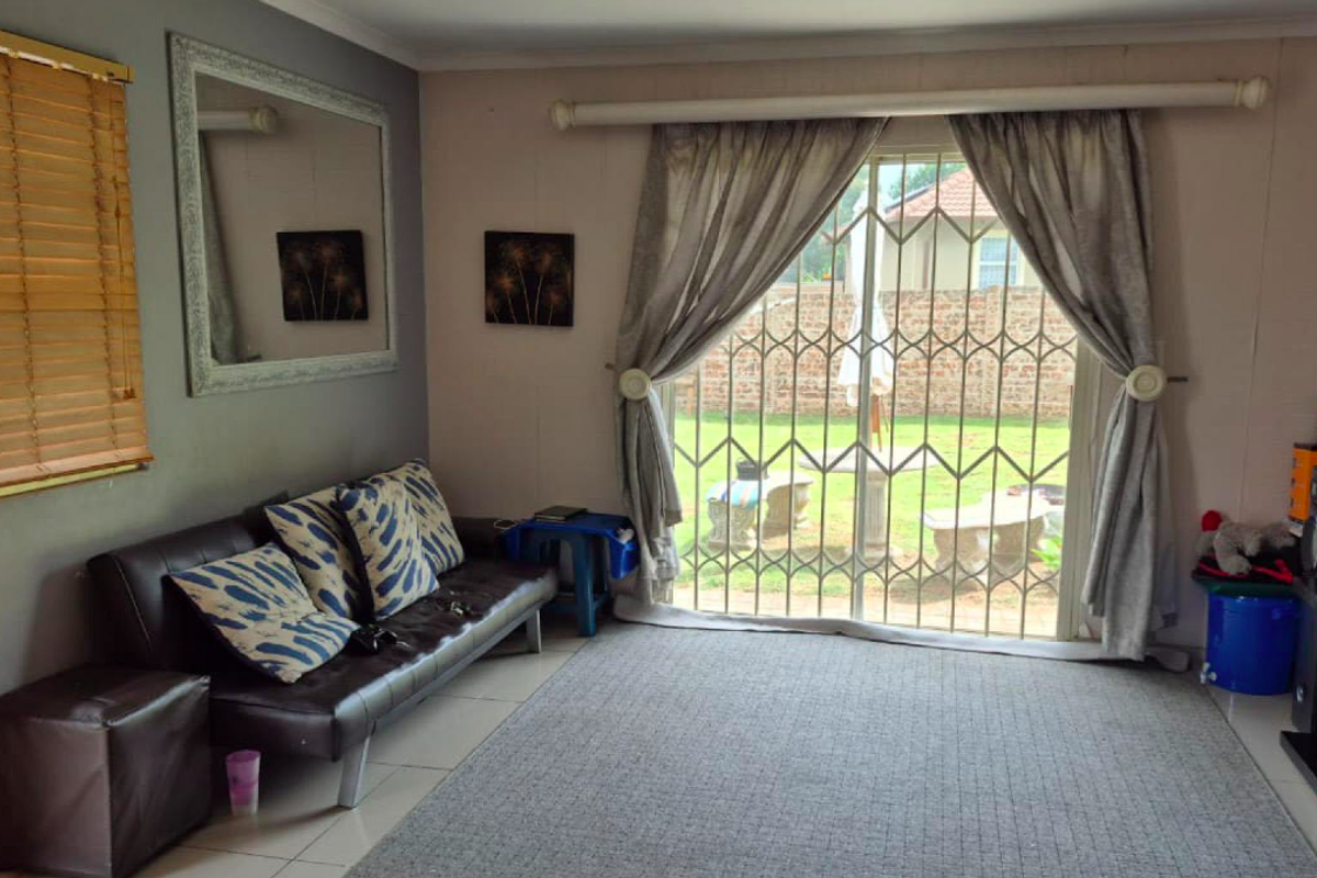 Living room featuring tiled flooring, venetian blinds, and a sliding glass door with a security gate providing access to the rear garden.