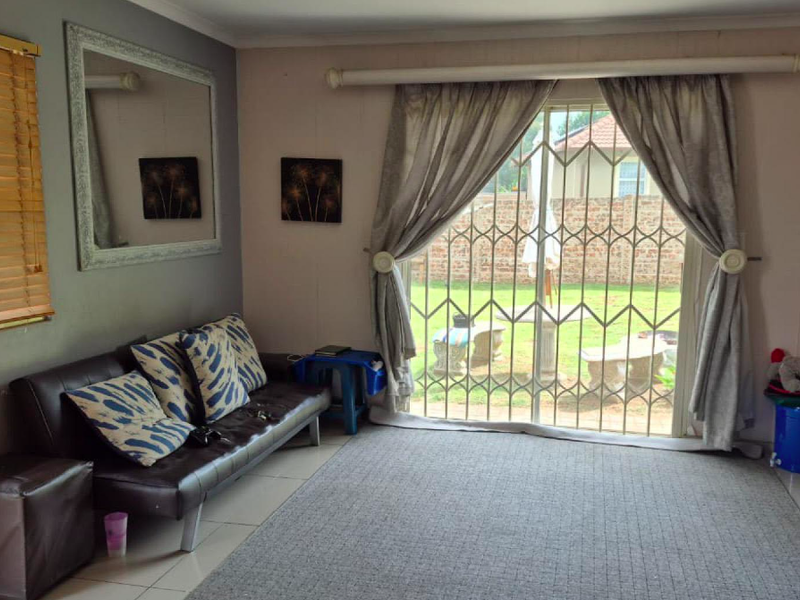 Living room featuring tiled flooring, venetian blinds, and a sliding glass door with a security gate providing access to the rear garden.