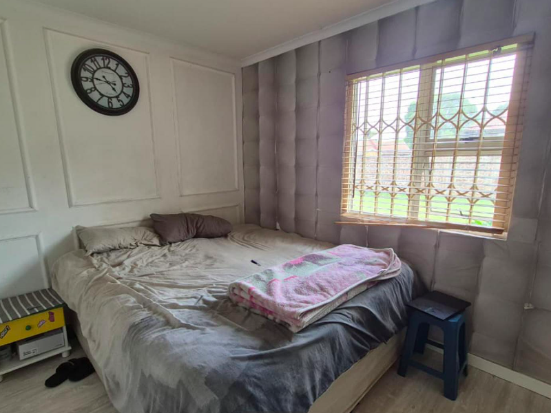 A bedroom featuring laminate flooring, decorative wall paneling, and a window fitted with a security gate.