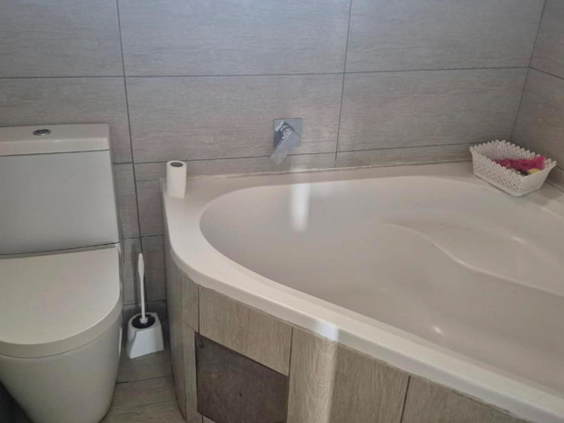 A functional bathroom featuring a corner bathtub with wall-mounted faucet and a modern toilet, finished with neutral ceramic wall tiling.