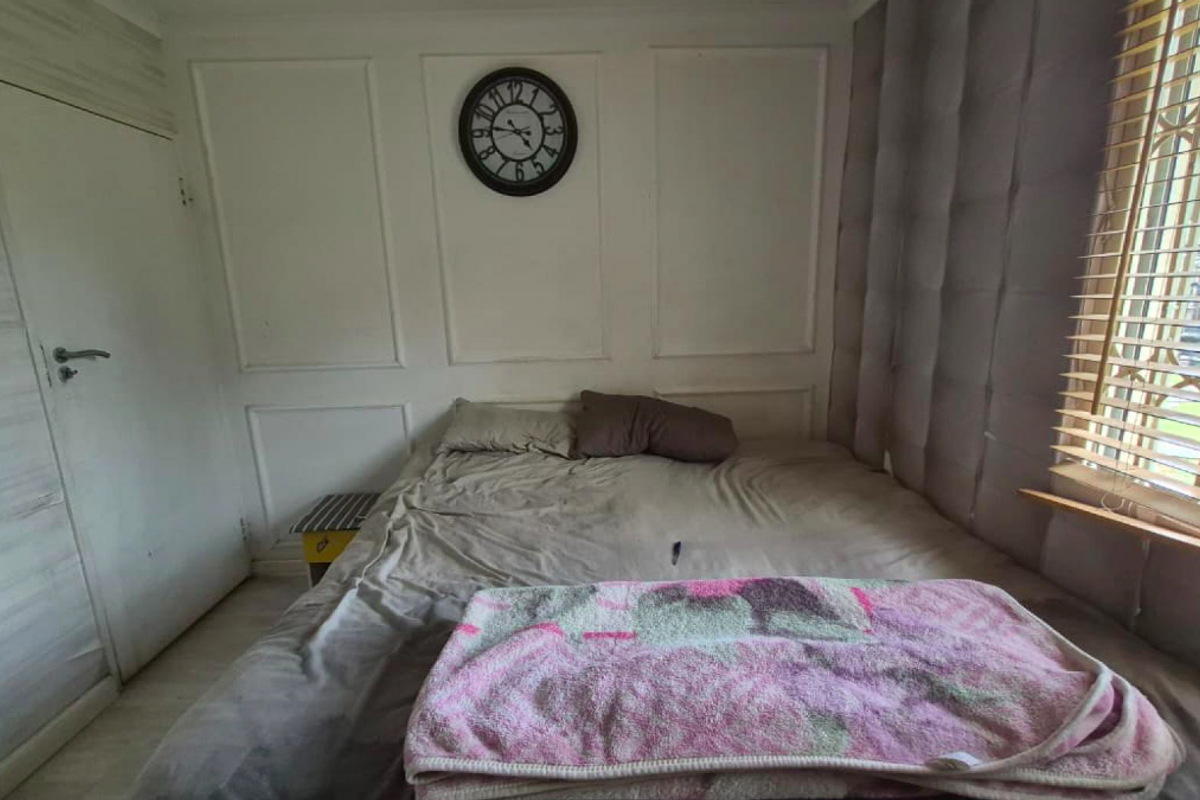 A bedroom featuring decorative wall paneling, window security bars, and venetian blinds.