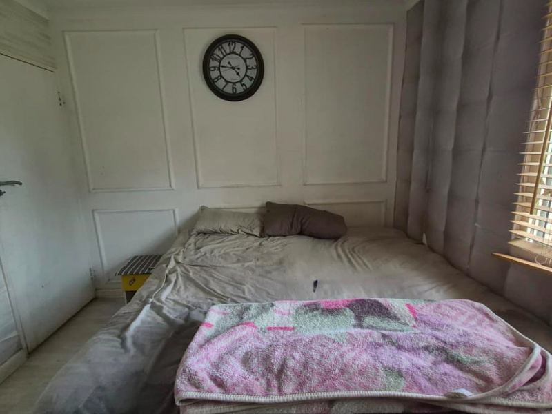 A bedroom featuring decorative wall paneling, window security bars, and venetian blinds.