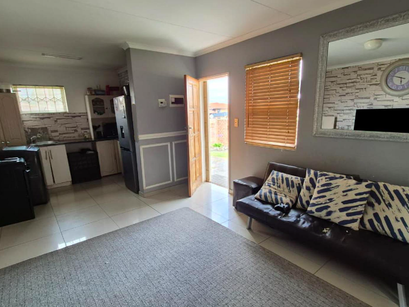 Open-plan living area featuring tiled flooring, wainscoting, and a compact kitchen space with built-in cabinetry and direct access to the exterior.