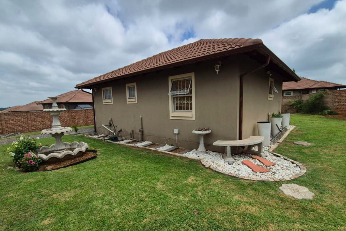 Rear view of the house featuring a tiled roof, landscaped garden area with stone accents, and a brick boundary wall.