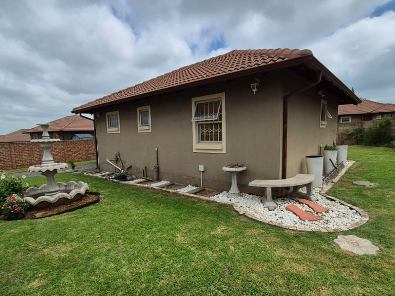 Rear view of the house featuring a tiled roof, landscaped garden area with stone accents, and a brick boundary wall.