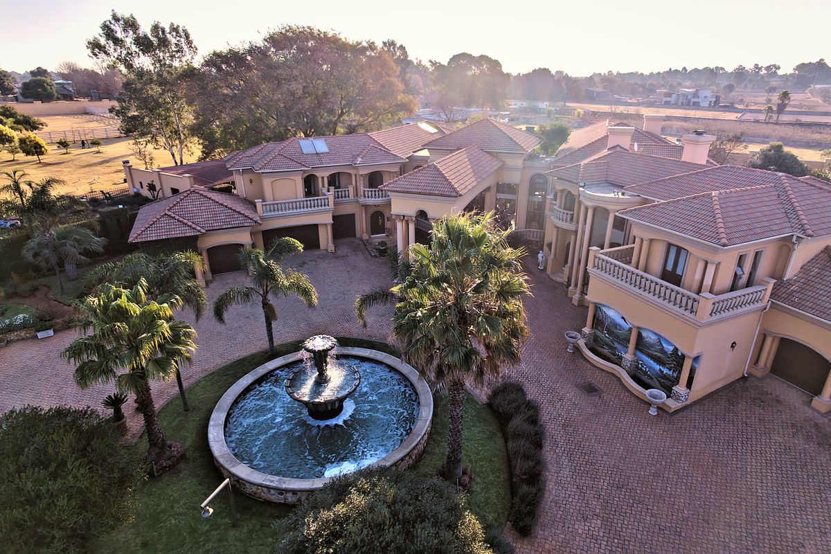 Aerial view of a large luxury residence featuring a paved courtyard, central water fountain, multiple garages, and extensive landscaped grounds.
