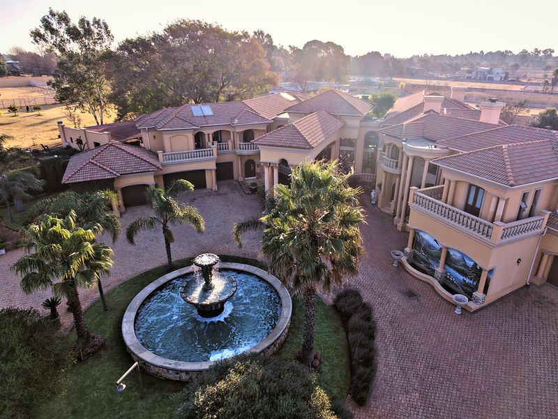 Aerial view of a large luxury residence featuring a paved courtyard, central water fountain, multiple garages, and extensive landscaped grounds.