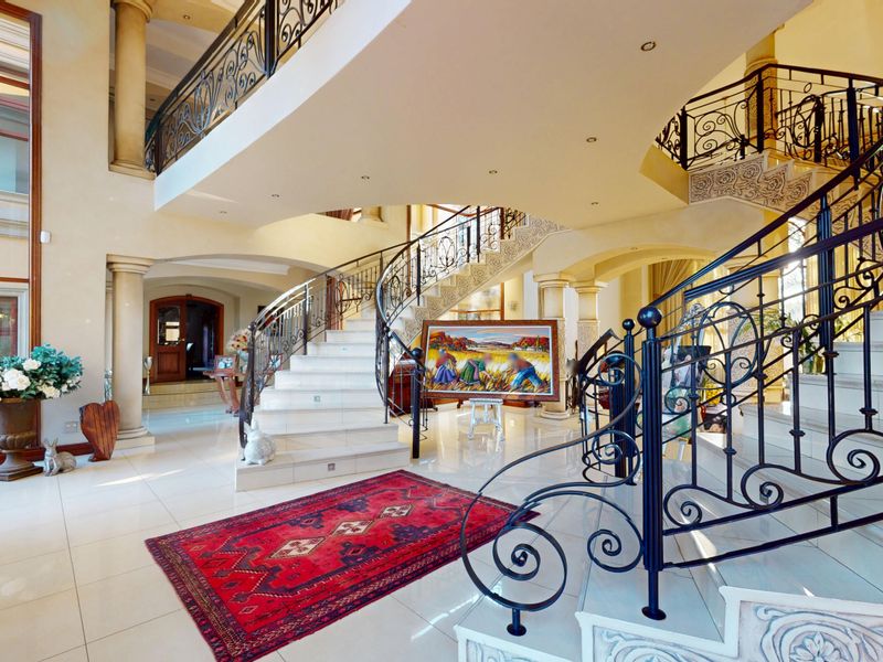 Grand entrance hall featuring a sweeping staircase with ornate wrought iron balustrades, polished marble flooring, and impressive double-volume ceilings.