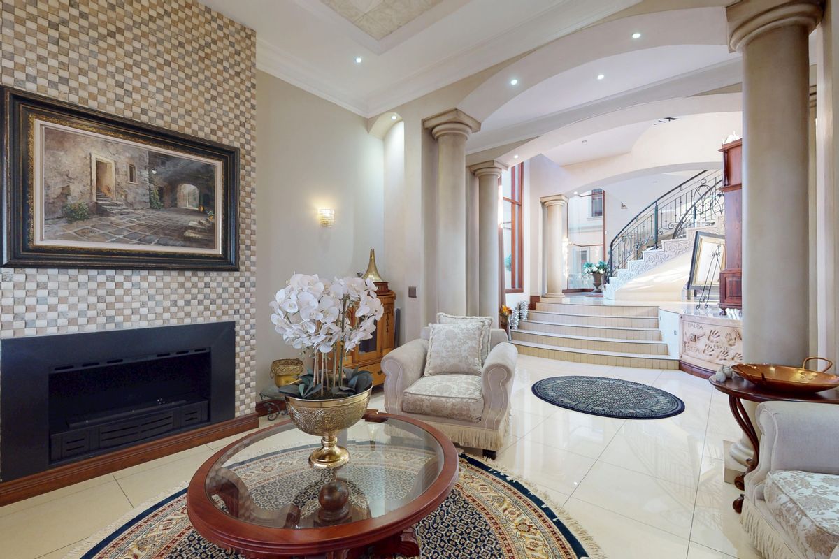 Elegant living room featuring a mosaic tile fireplace, polished tile floors, decorative columns, and a grand staircase with wrought iron detailing.