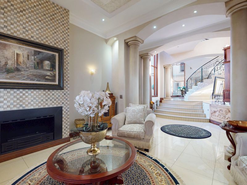 Elegant living room featuring a mosaic tile fireplace, polished tile floors, decorative columns, and a grand staircase with wrought iron detailing.
