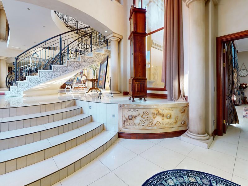 Grand entrance hall featuring a sweeping curved staircase with ornate wrought iron balustrades, polished tile flooring, and elegant architectural columns.