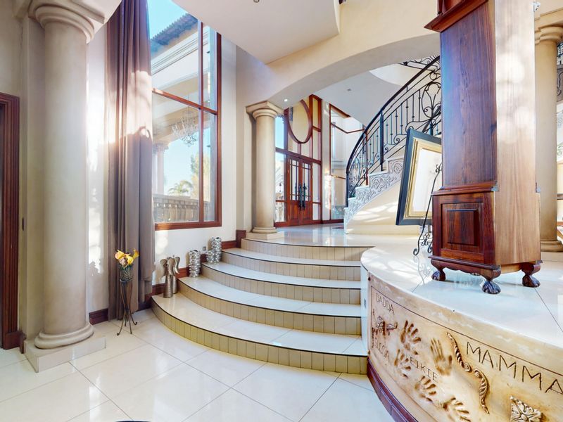 Grand entrance hall featuring a sweeping curved staircase with wrought iron balustrade, tiled flooring, and impressive double-height windows providing abundant natural light.
