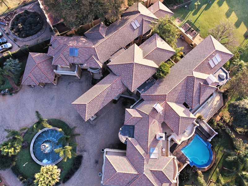 Aerial view of a large residential property featuring a complex tiled roof structure, swimming pool, paved driveway, and landscaped grounds.